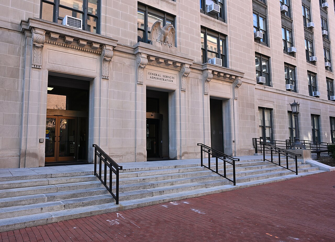 The entrance to the General Services Administration building with a stone facade, large stone steps leading up to two doorways, and an eagle sculpture above the central doorway.