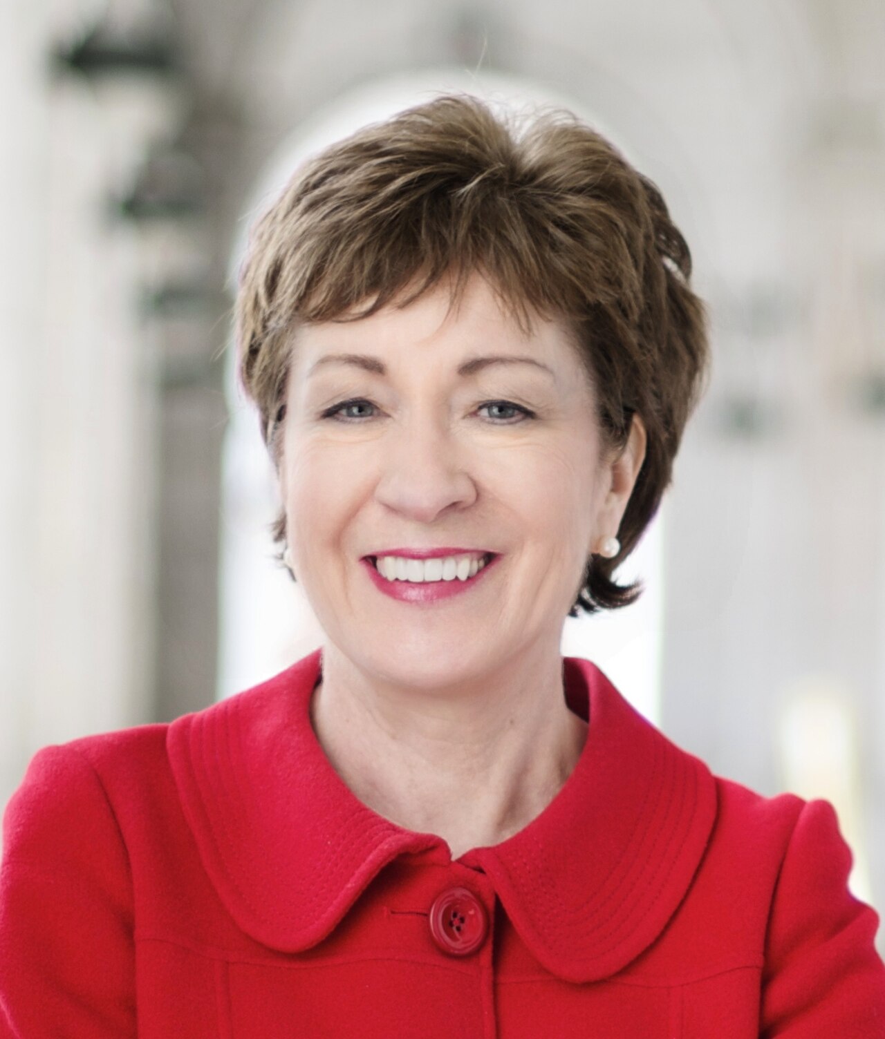 A smiling middle-aged woman with short brown hair wearing a red collared jacket