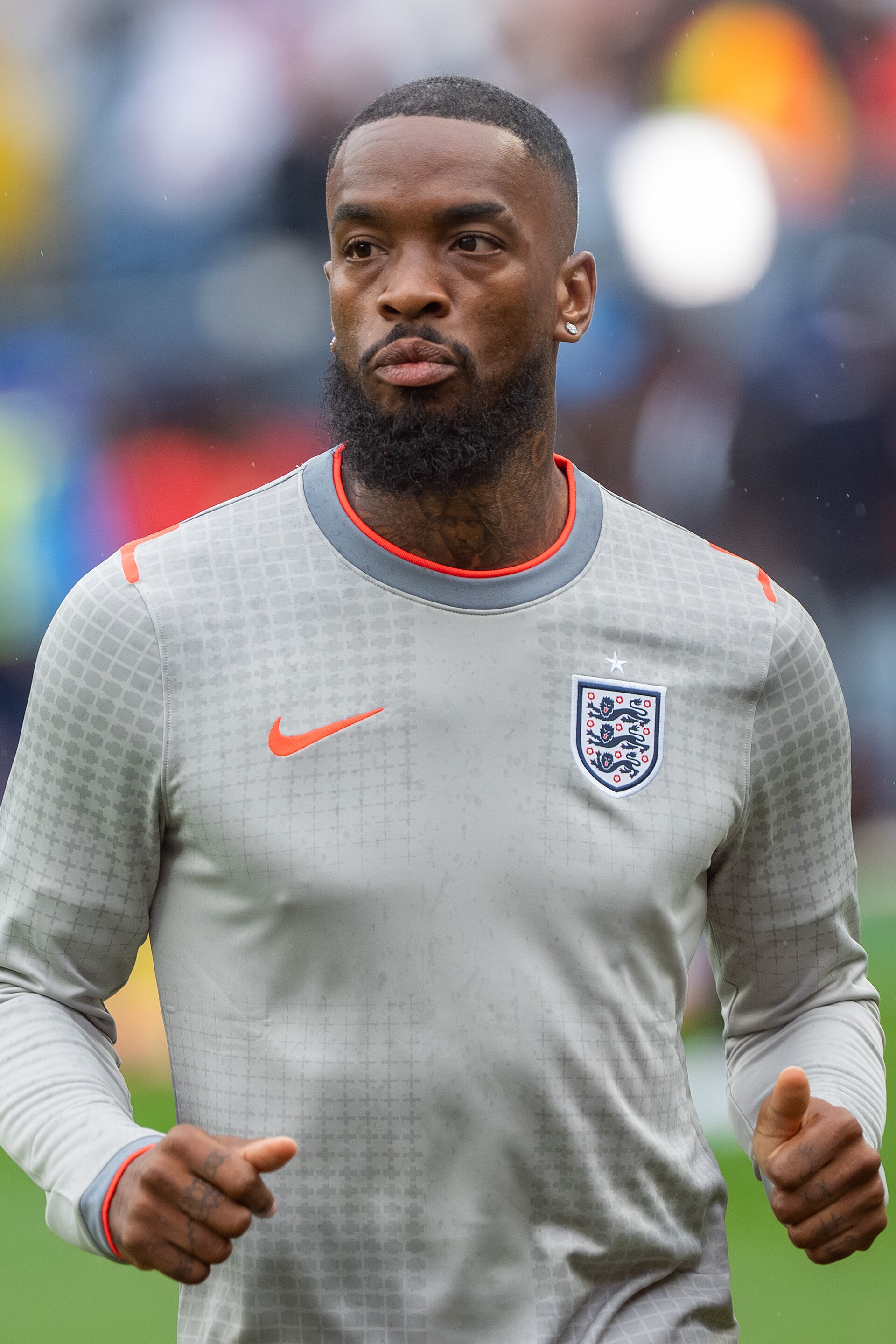 England striker Ivan Toney in a gray England jersey with an orange Nike checkmark and a blue shield with three lions on the chest, running on a green field.
