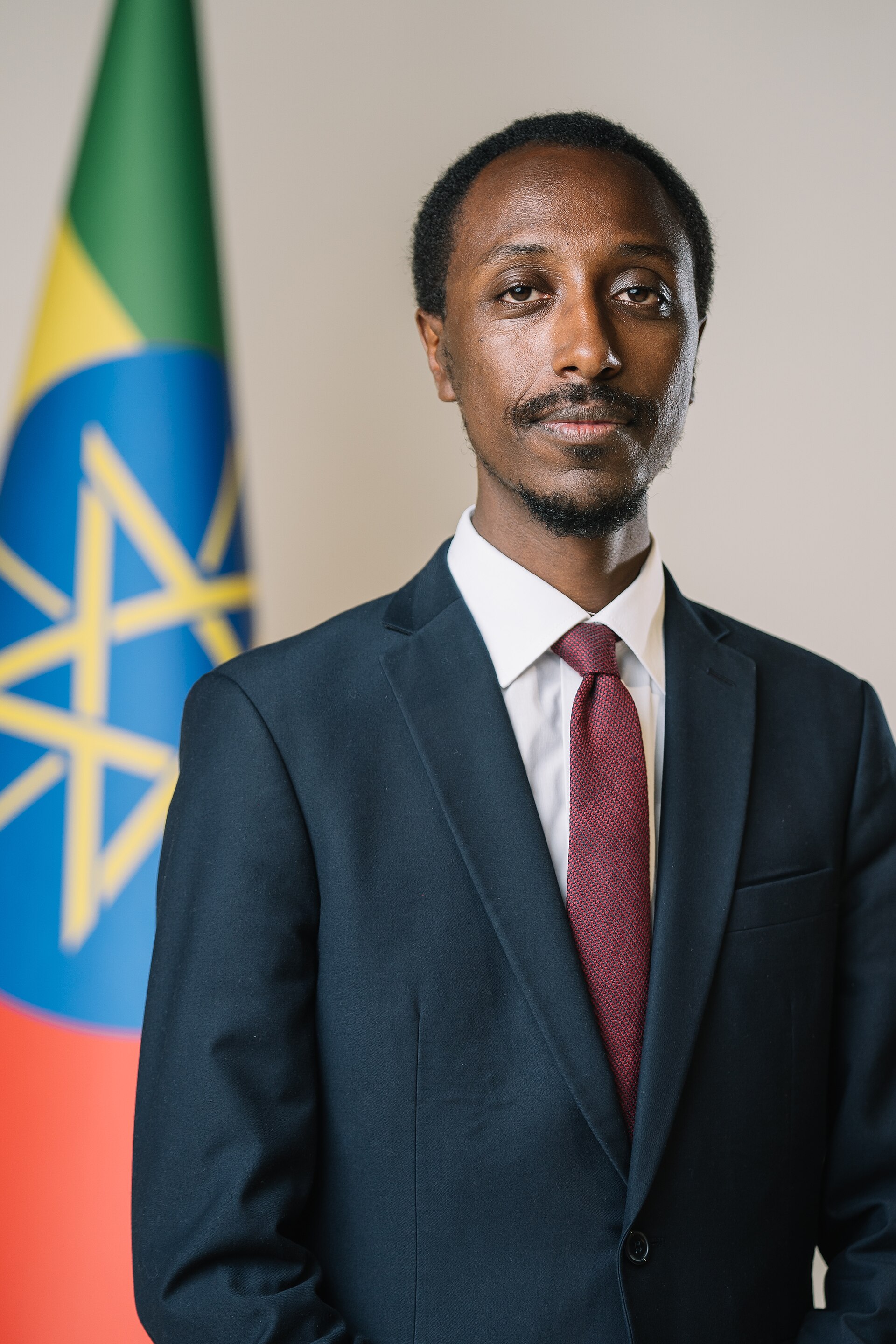 A man in a suit standing in front of a flag