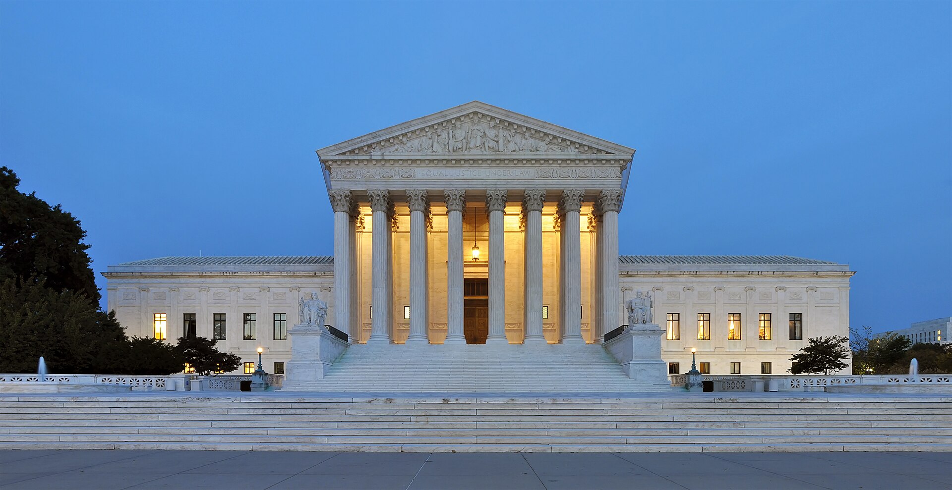 The Supreme Court building in Washington D.C. at dusk, with its grand staircase, columns, and pediment illuminated.