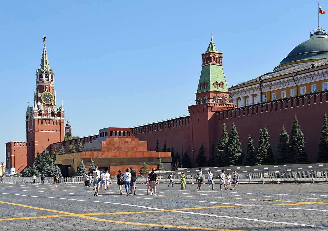 Red Square in Moscow, with the Kremlin wall, Spasskaya Tower, and Lenin Mausoleum under a clear sky.