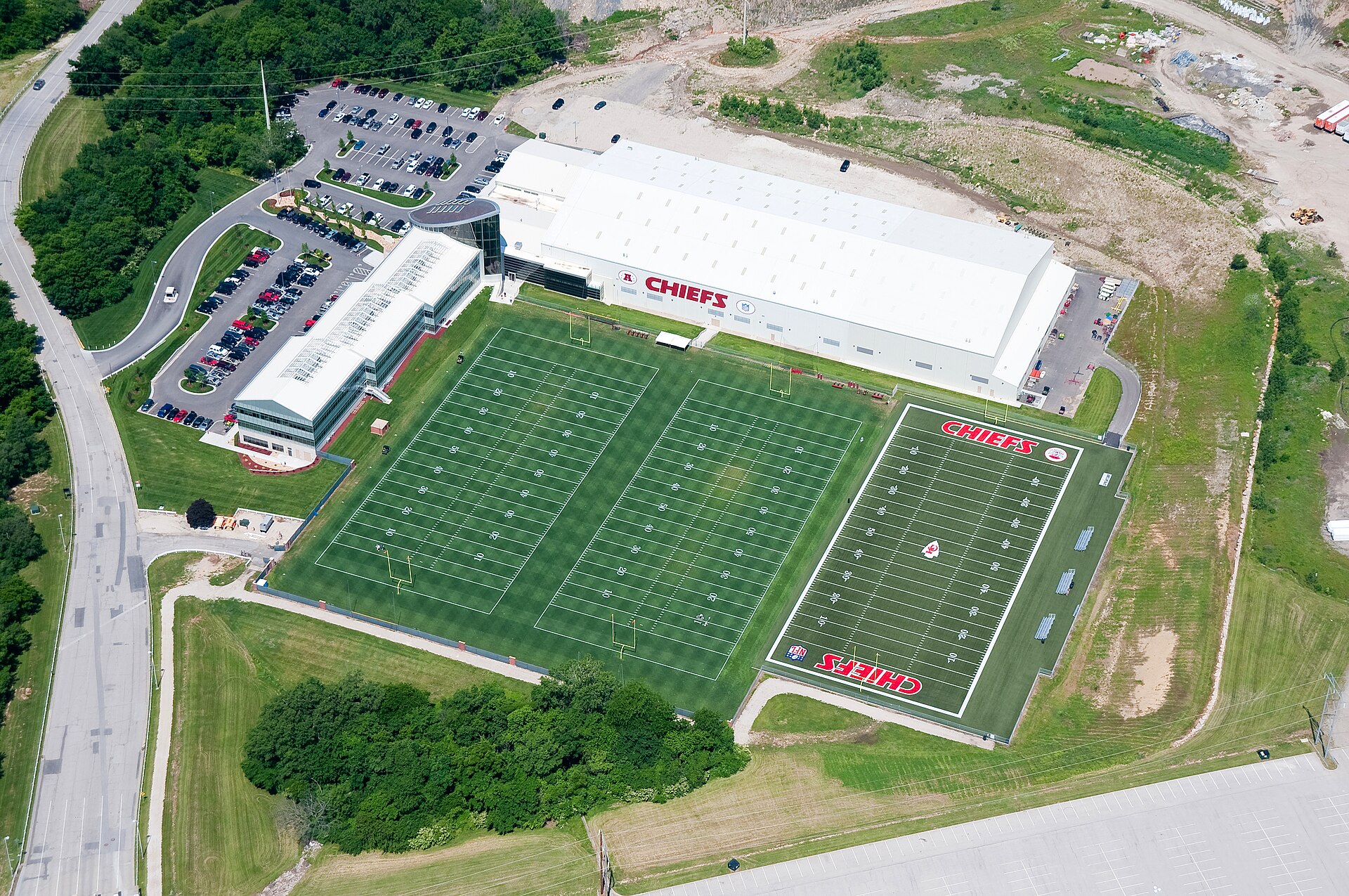 Aerial view of a football practice facility with two green fields and a large white building labeled 'CHIEFS' in red.