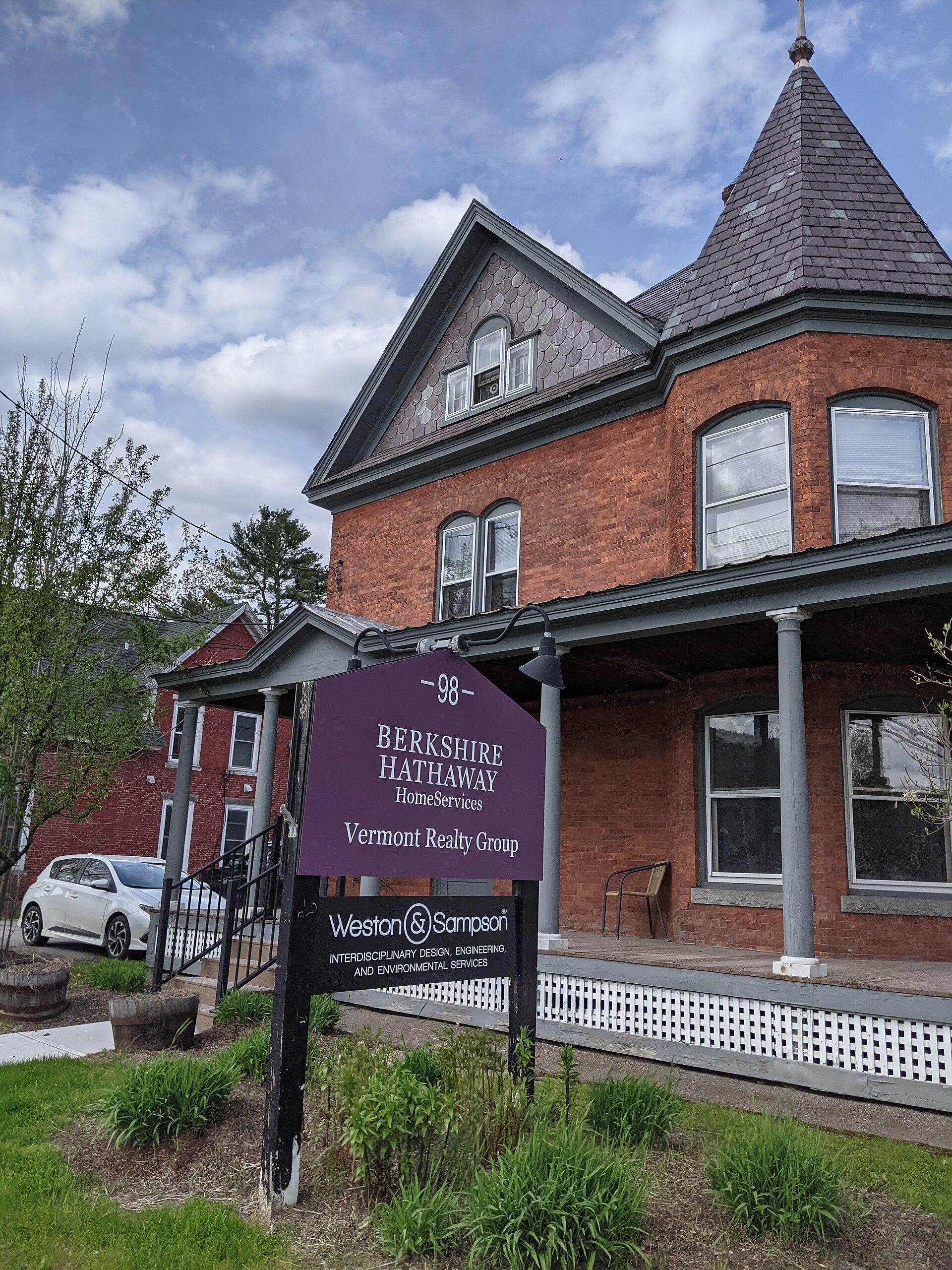 A sign for Berkshire Hathaway HomeServices Vermont Realty Group is displayed in front of a brick building.
