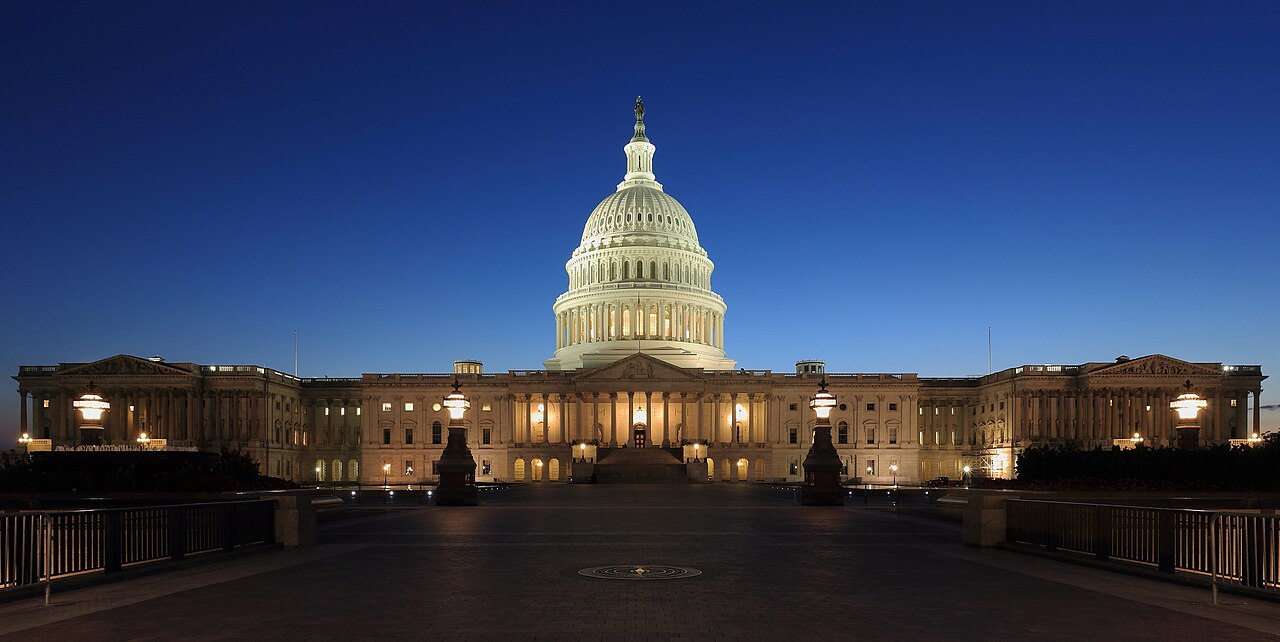The United States Capitol building at dusk with its dome and columns illuminated against a dark blue sky