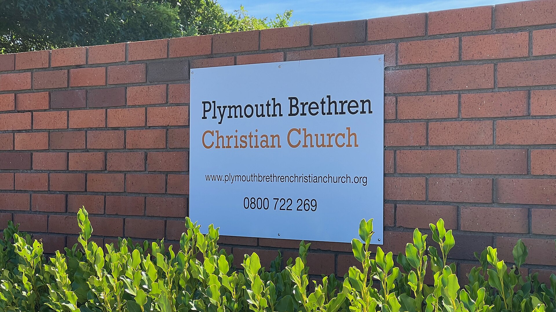 A sign on a brick wall reads "Plymouth Brethren Christian Church" with a website and phone number below.