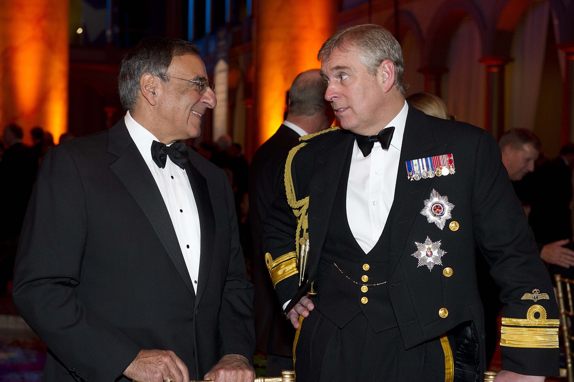 Prince Andrew in a formal black naval uniform with medals talking to another man in a tuxedo