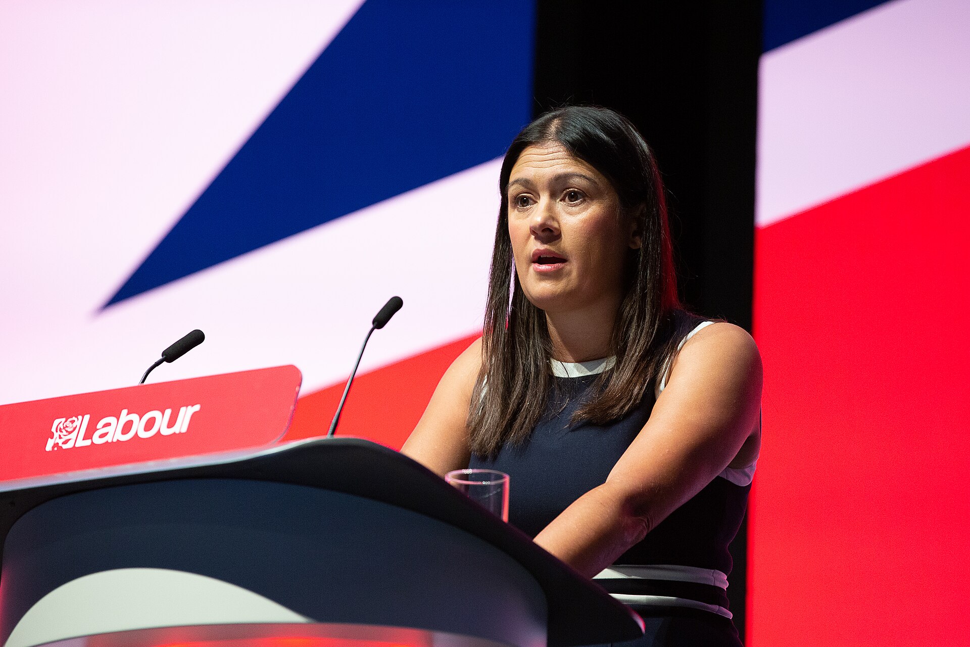 Lisa Nandy speaks at a podium with a Labour logo on it, with a red and blue background.