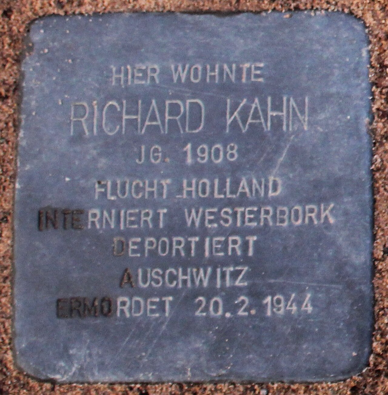 A Stolperstein (stumbling stone) with the inscription 'HIER WOHNTE RICHARD KAHN JG. 1908 FLUCHT HOLLAND INTERNIERT WESTERBORK DEPORTIERT AUSCHWITZ ERMORDET 20.2.1944'.