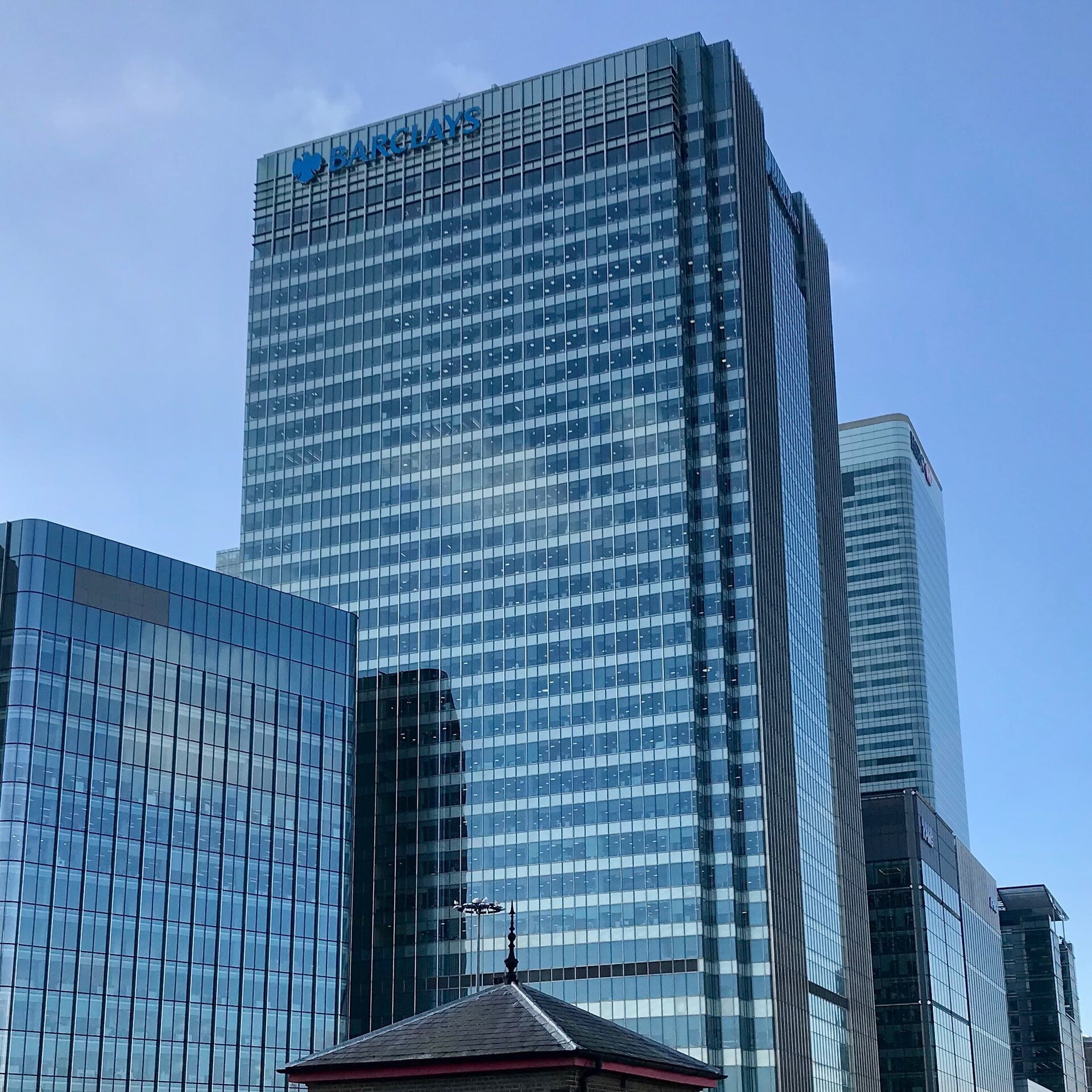 A tall glass skyscraper with the Barclays logo and name visible at the top, under a clear blue sky.