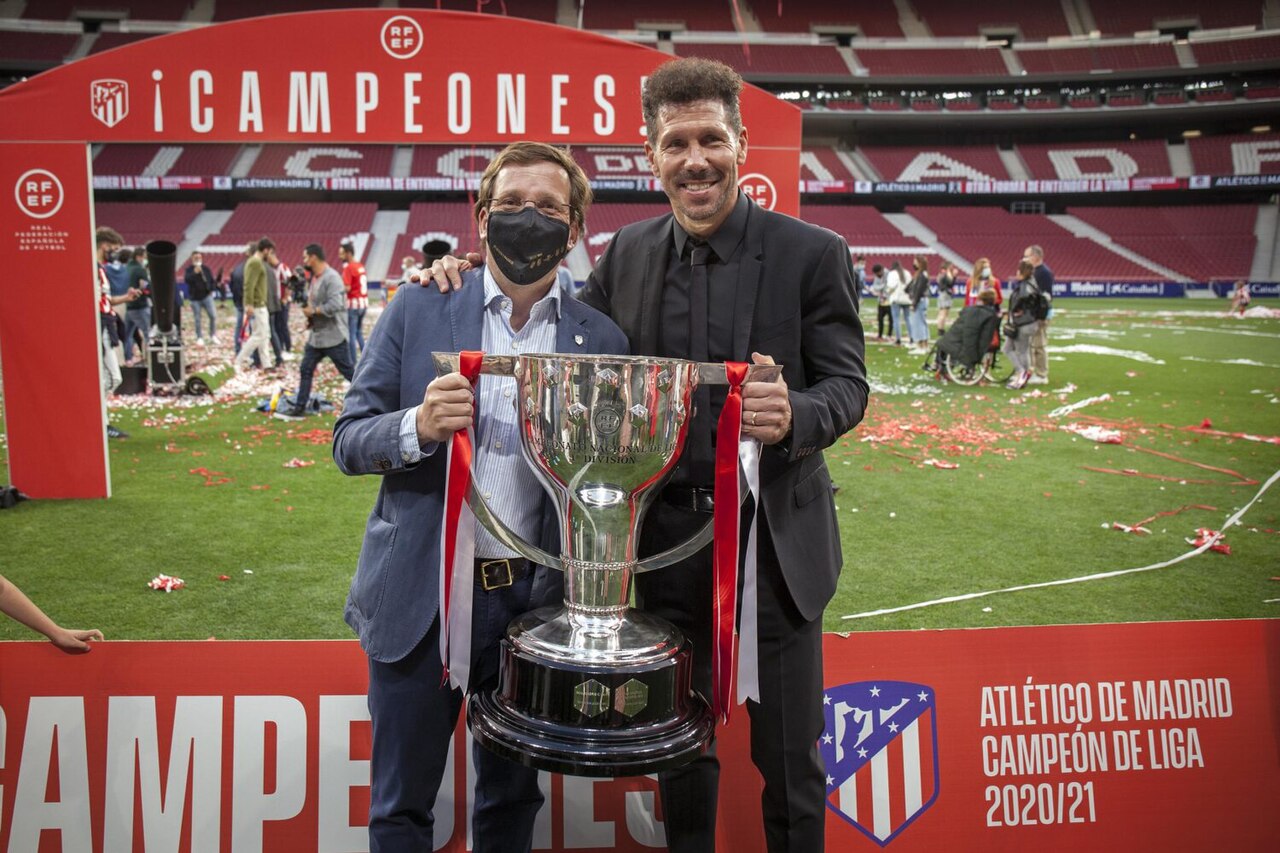 Two men holding a trophy on a football field with confetti and banners.