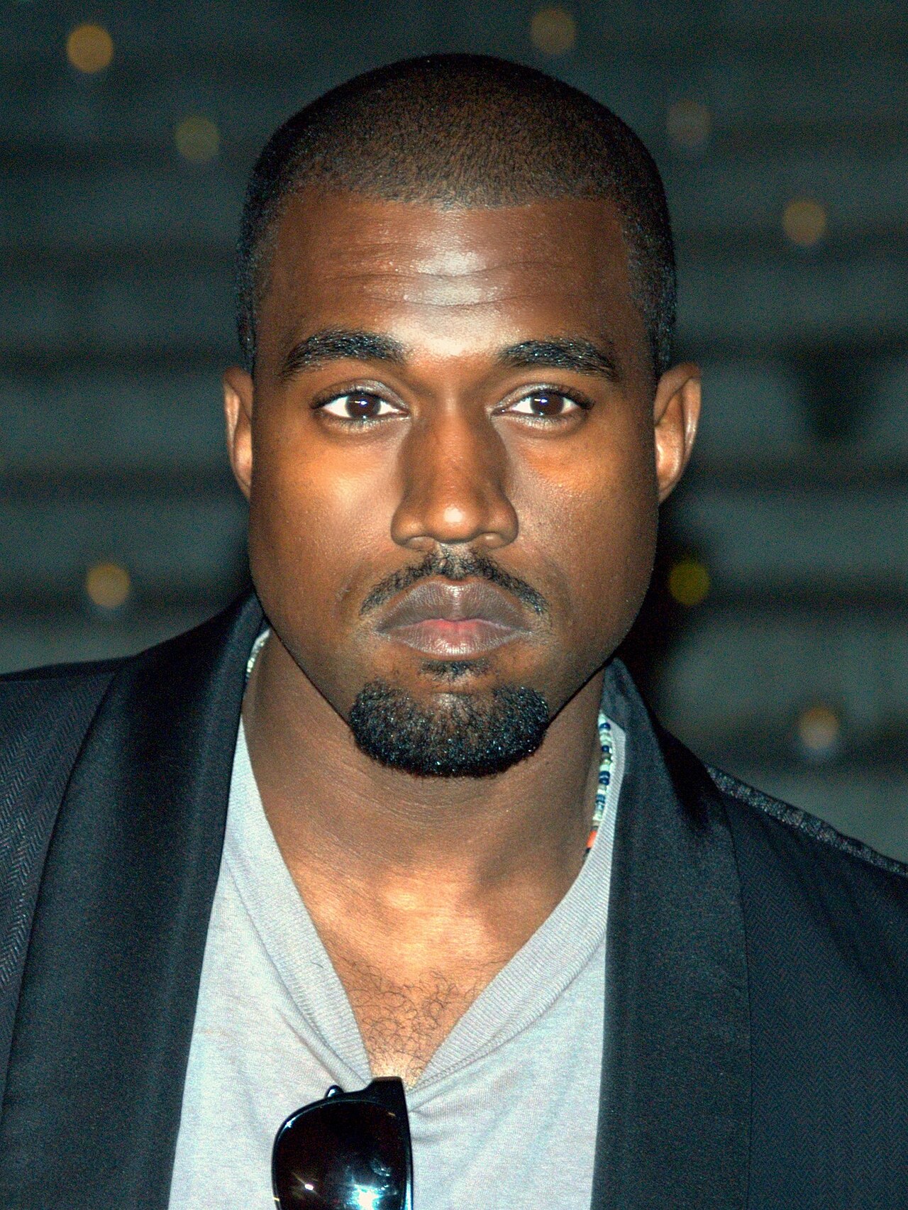 A close-up photo of Kanye West, a Black man with short hair, wearing a gray shirt and black jacket.