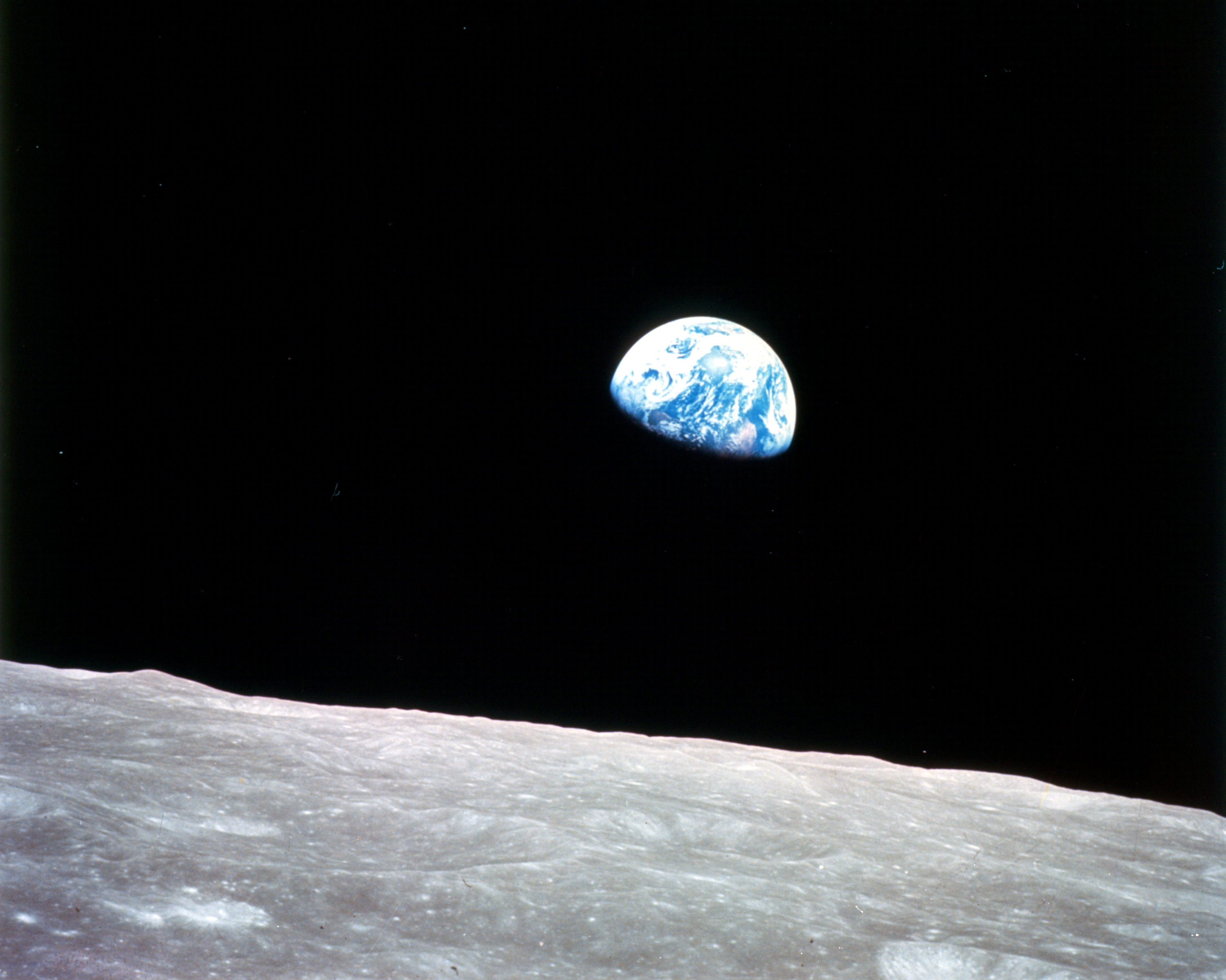 This view of the rising Earth greeted the Apollo 8 astronauts as they came from behind the Moon after the fourth nearside orbit. Earth is about five degrees above the horizon in the photo. The unnamed surface features in the foreground are near the eastern limb of the Moon as viewed from Earth. The
