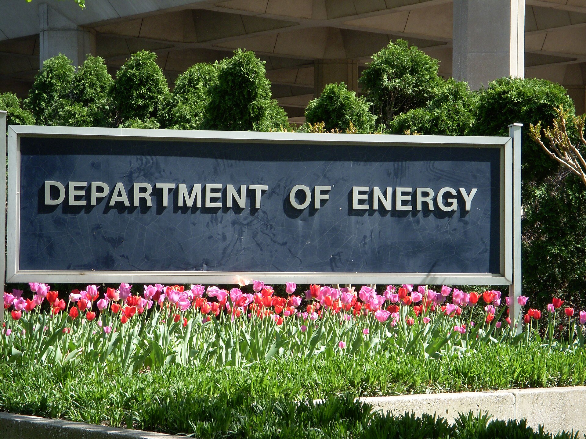 A sign that reads 'DEPARTMENT OF ENERGY' is displayed in front of manicured bushes and a bed of colorful tulips.
