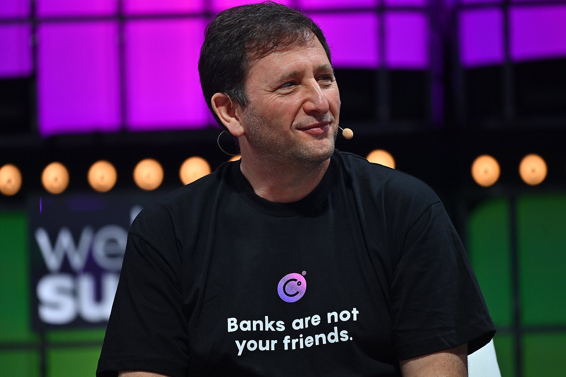 A man with short dark hair wearing a black t-shirt with a logo and the text 'Banks are not your friends.'