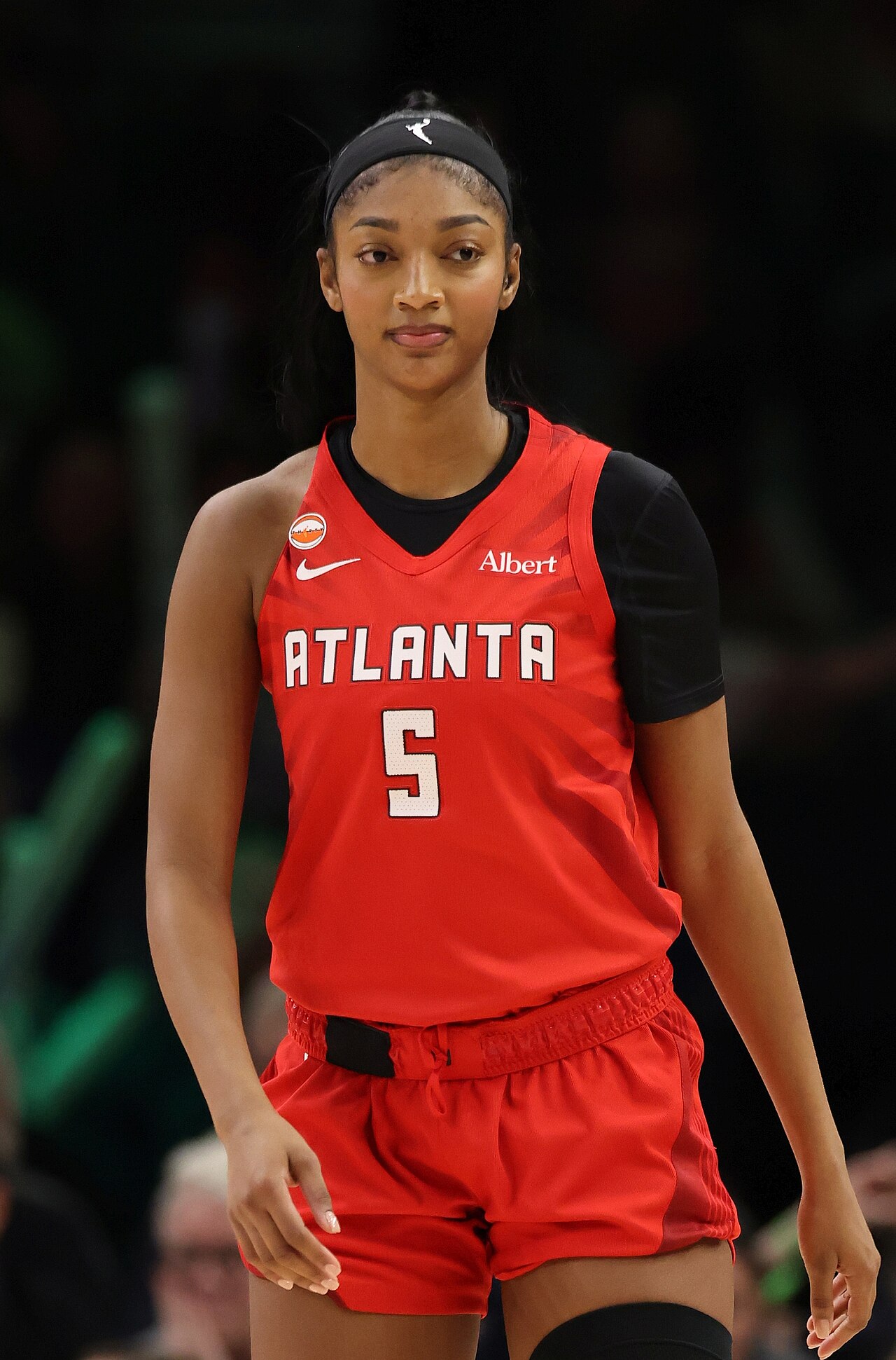 A woman in a red Atlanta jersey with the number 5 and black shorts and headband looks ahead with her hands at her sides.
