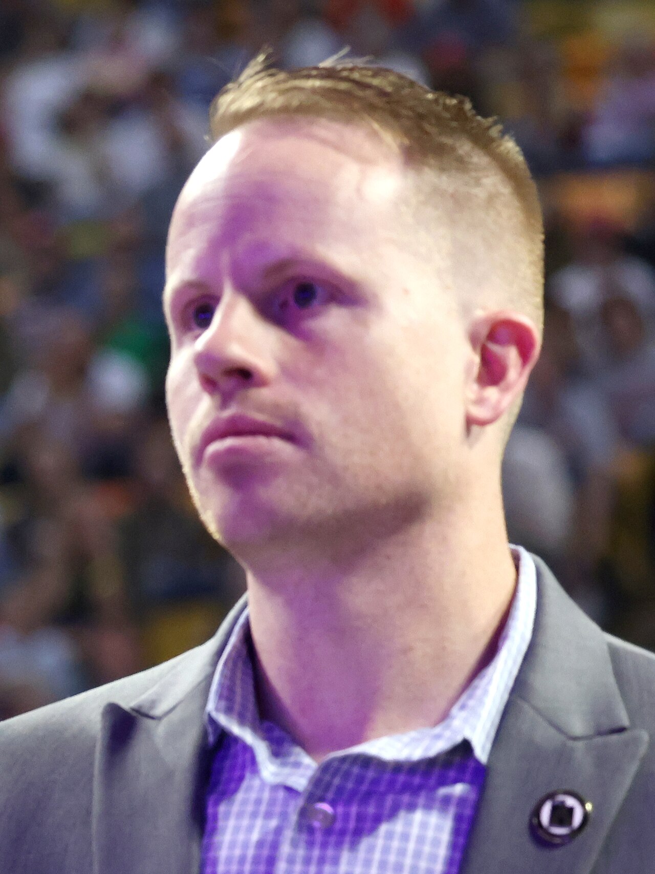Close-up portrait of Trevor Lee, a man with short blond hair wearing a gray blazer and checkered shirt, with a Utah flag pin on his lapel