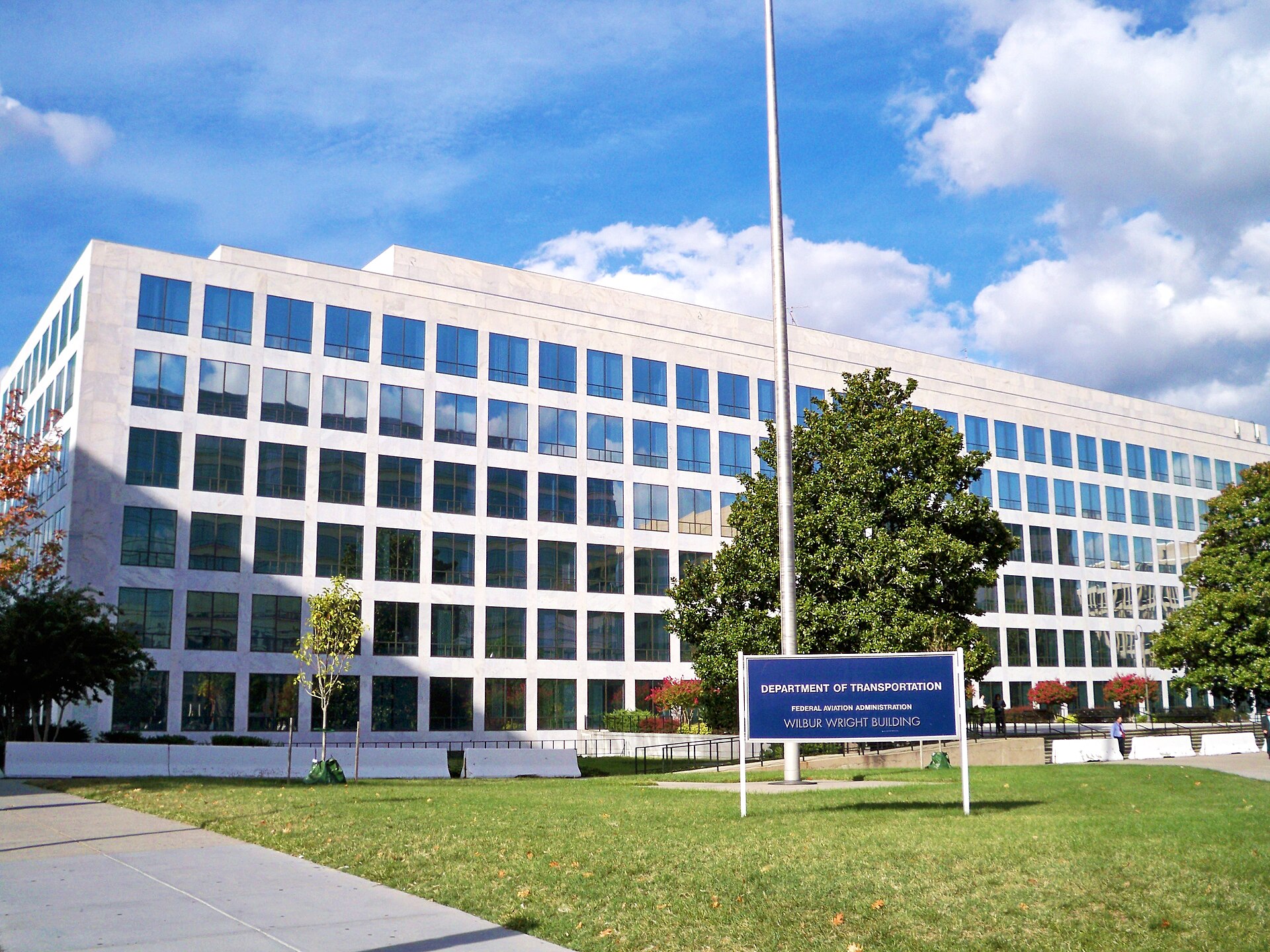 A large white building with many windows and a blue sign that reads Department of Transportation, Federal Aviation Administration, Wilbur Wright Building.