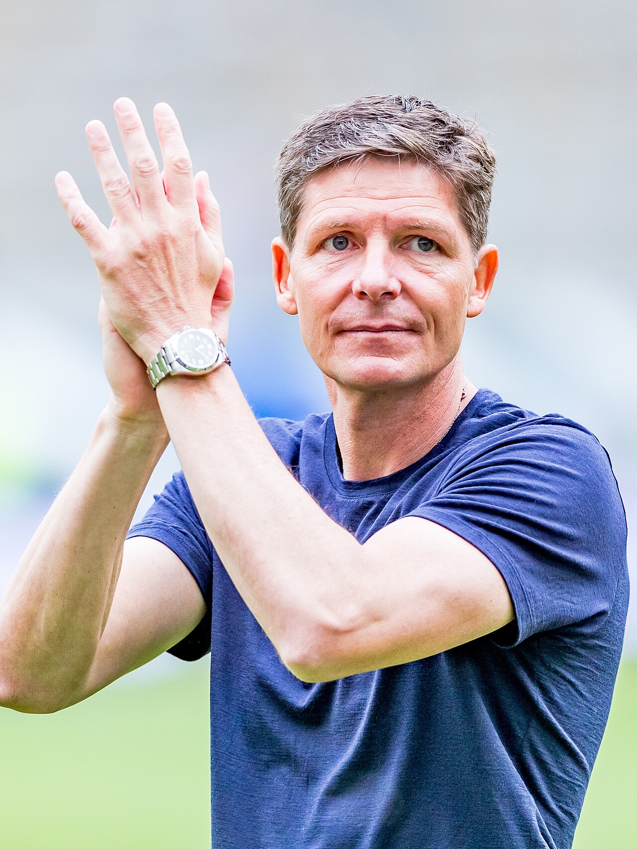 A man with short hair wearing a blue t-shirt and a watch, clapping.